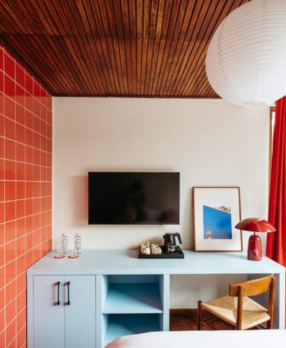 Bright hotel room with orange tiles, cosy wooden chair, modern TV, and a coffee station for a relaxing stay.