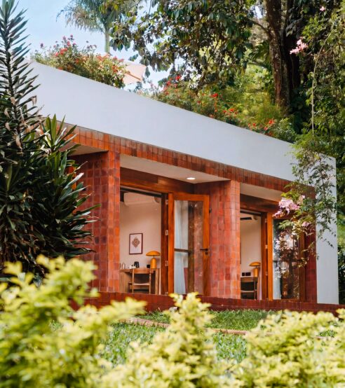 Bright hotel room with floor-to-ceiling windows, lush garden views, and inviting seating area, perfect for relaxation.